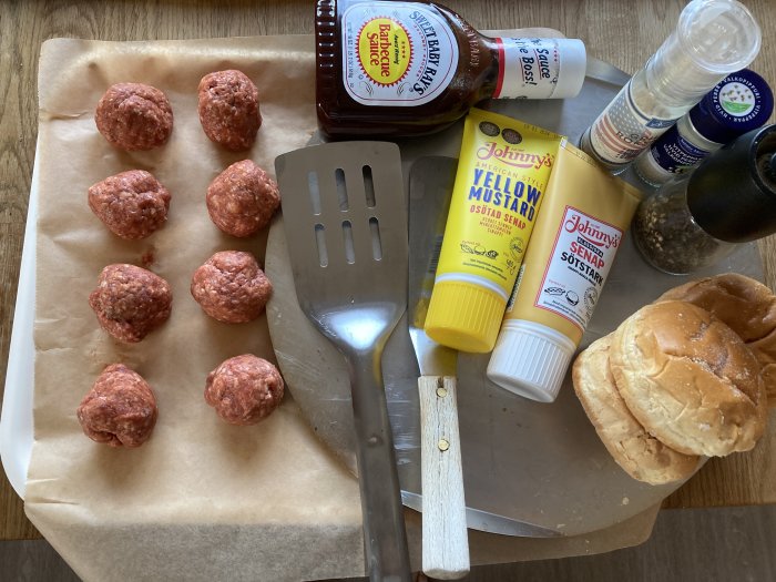 Köttbullar, hamburgerbröd, tillbehör som ketchup, senap, och kryddor, stekspade på skärbräda, måltidsförberedelse.