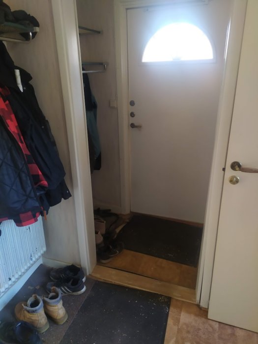 En hall med ytterdörr, klädhängare, skor, och en vit vägg.