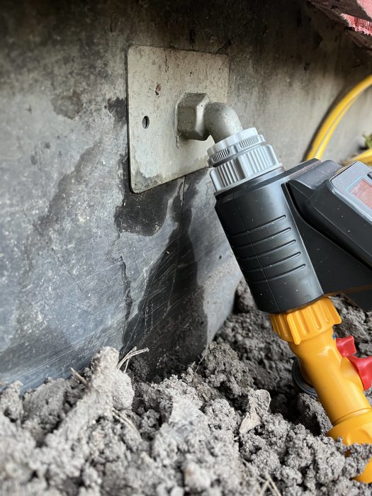 Elverktyg anslutet till utomhusuttag, på marken, omgivet av smuts och grå betongyttervägg.