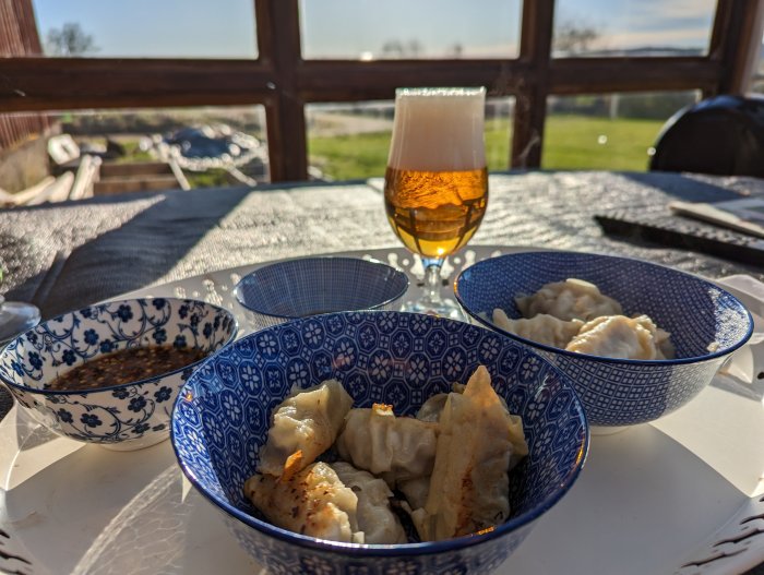 Dumplings i skålar, ölglas, solljus, uteservering, landskap bakgrund, avslappnad måltid.