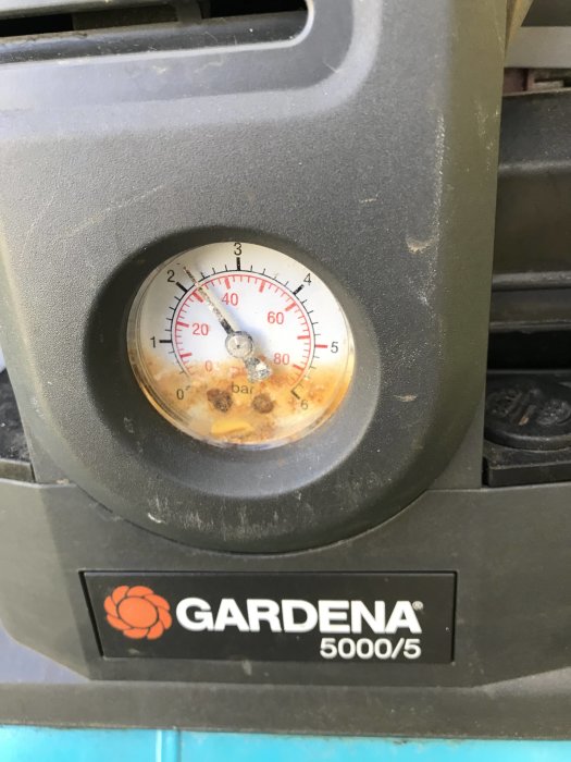 Manometer på Gardena-utrustning visar tryck, damm och rost; logotyp synlig nedtill.