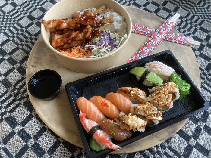 Asiatisk maträtt med sushi och yakitori över ris, sojasås, på rutig duken.