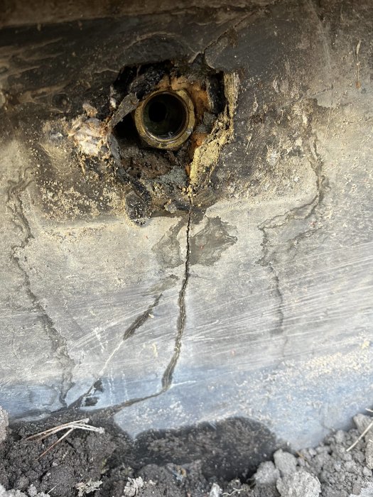 Bild på skadat fordonsgolv med rost, hål och sprickor runt ett rör- eller bultuttag.