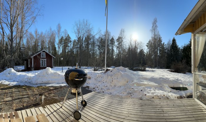 Trädäck med grill, röd stuga, smältande snö, skogsmark, soligt, klart väder, svensk landsbygd på våren.