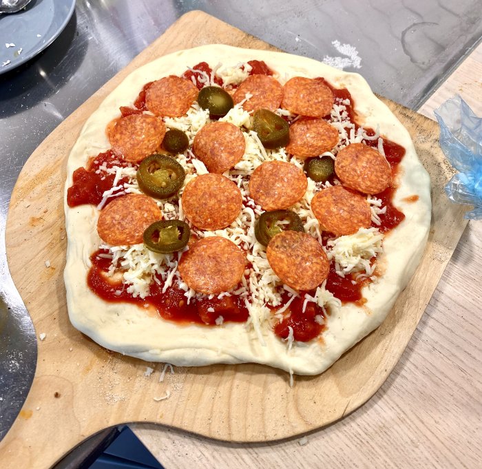 Ogräddad pizza på träskärbräda med pepperoni, jalapeños och riven ost.