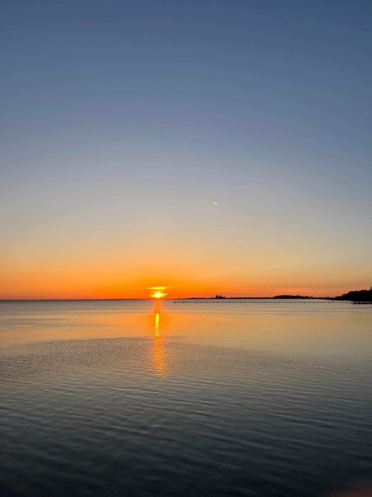 Solnedgång över havet, orange himmel, reflektion på vattenytan, lugnt, fredligt.