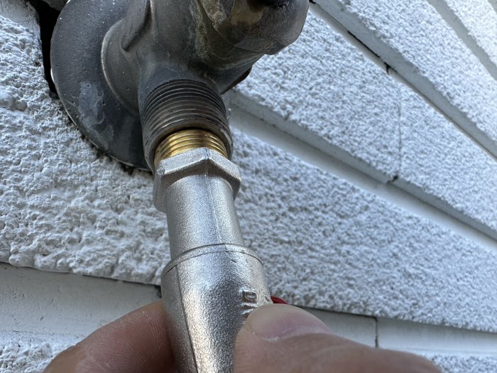 Ansluter en metallslangkoppling till en utomhuskran, hand synlig, träväggsidobakgrund.