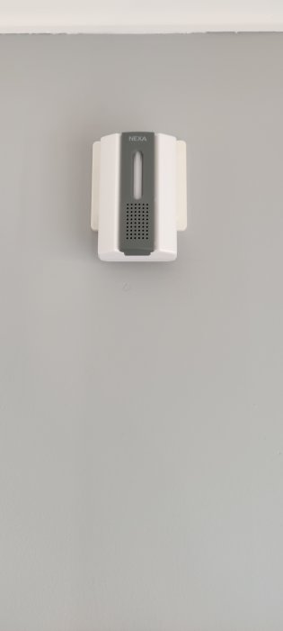 En vit Nexa-enhet monterad på en gråvägg med minimalistisk design.