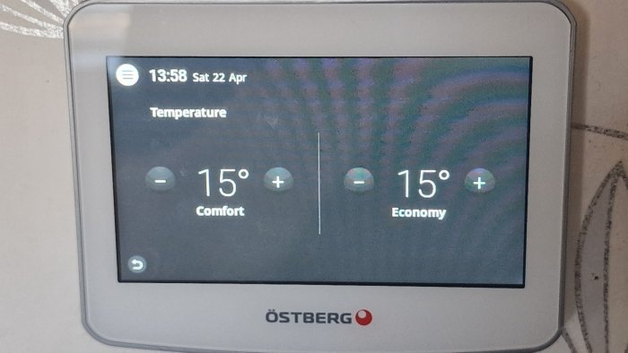 Digital termostat visar 15 grader för både "Comfort" och "Economy", tid och datum i övre vänstra hörnet.