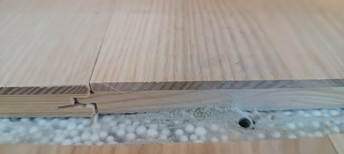 Två träskivor, en med skår, en ovanpå cellduk med polystyrenkulor, detaljbild av byggnadsmaterial.