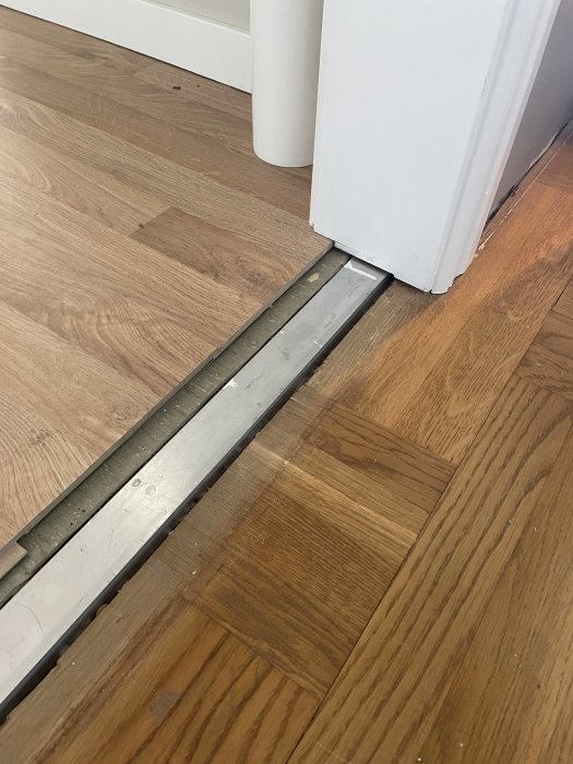 En metalltröskel mellan två olika trägolvtyper vid en dörröppning i ett hem.