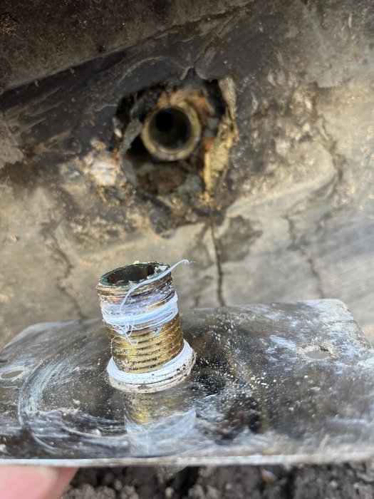 Metallrör med gängor avbruten, tätningsmaterial. Defekt rördel, skadad, behov av reparation. Smutsig bakgrund.