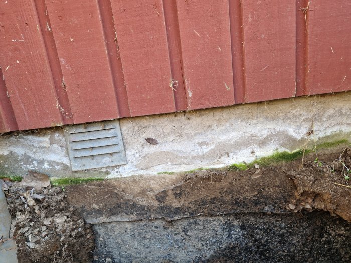 Röd vägg, ventilation, erosion vid grund, synlig betong, grön mossa, jord och grus.