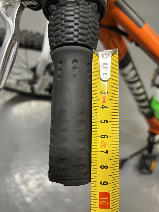 Cykelhandtag bredvid måttband, mäter cirka fem centimeter tjocklek, detalj av cykel.