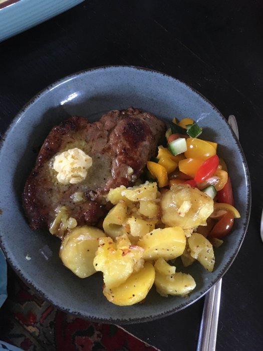 En tallrik med stekt kött, smörklick, potatisskivor och blandad grönsakssallad.