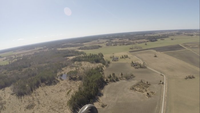 Flygfoto över ett lantligt landskap med åkrar, skog och vägar på en solig dag.