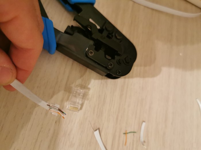 Hand med krimpåsattång, förbereder nätverkskabel med RJ45-kontakt. Arbetsyta med kabelskrot.