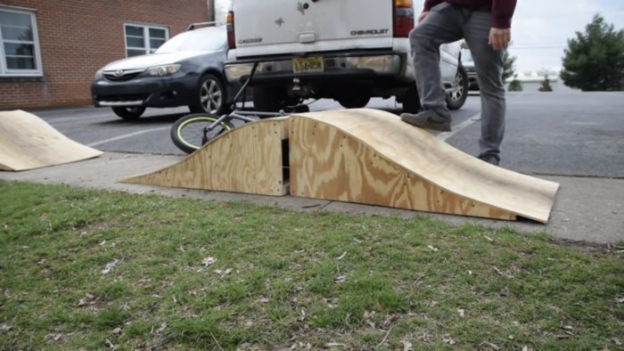 Träramp för skateboard eller BMX, bilparkering, person, gräs och asfalt, bakre delen av en SUV.