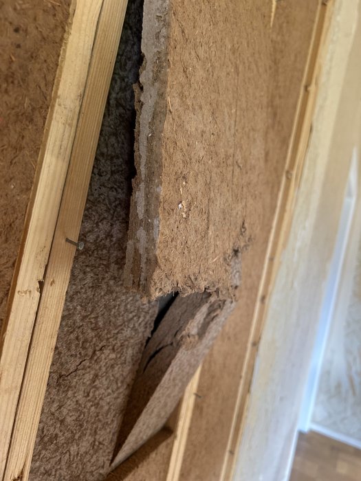 Närbild på skadad vägg med exponerad isolering och träreglar i en byggnad eller renovering.