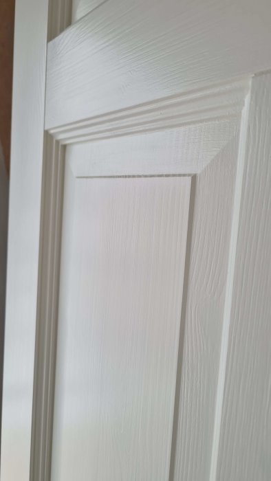 Vit målad träpanel, närbild, dörr- eller fönsterkarmstruktur, detaljer i snickeri.