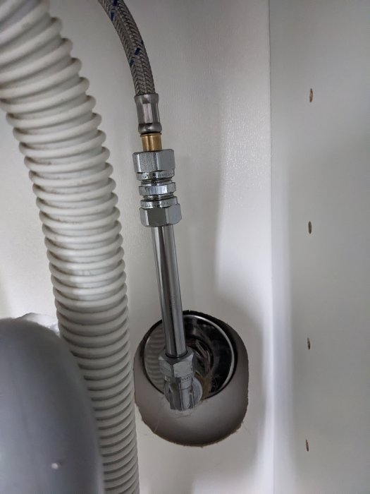 Vattentillförselslang, ansluten till armatur, genom vägg, flexibel avloppsslang, vit bakgrund, installation, VVS.