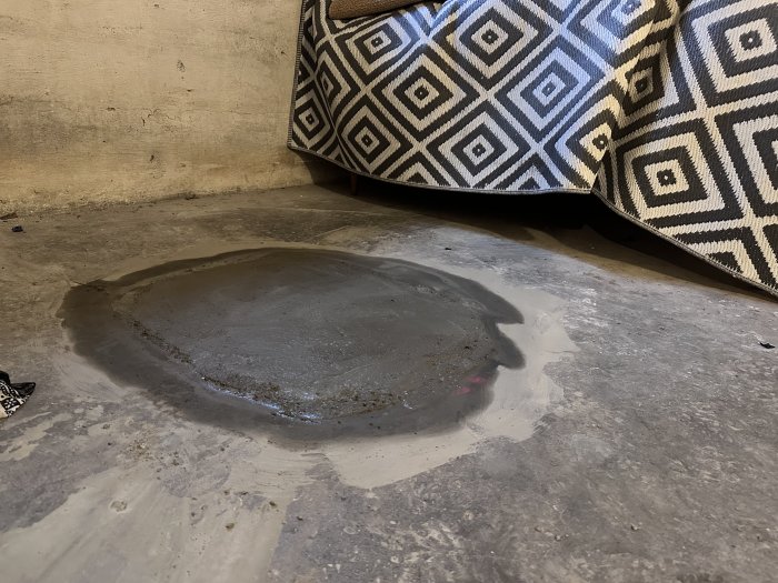 En stor vattenpöl på ett betonggolv med mönstrad soffkant i hörnet.