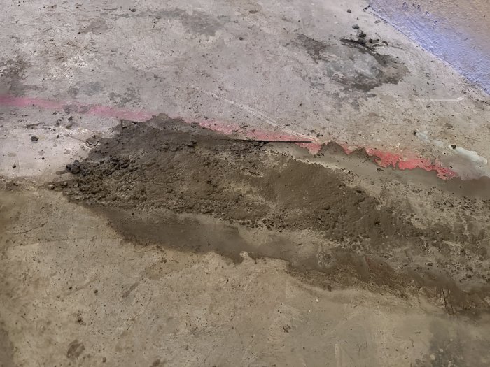 Slitet betonggolv med sprickor, smuts, och en röd färgmarkering.
