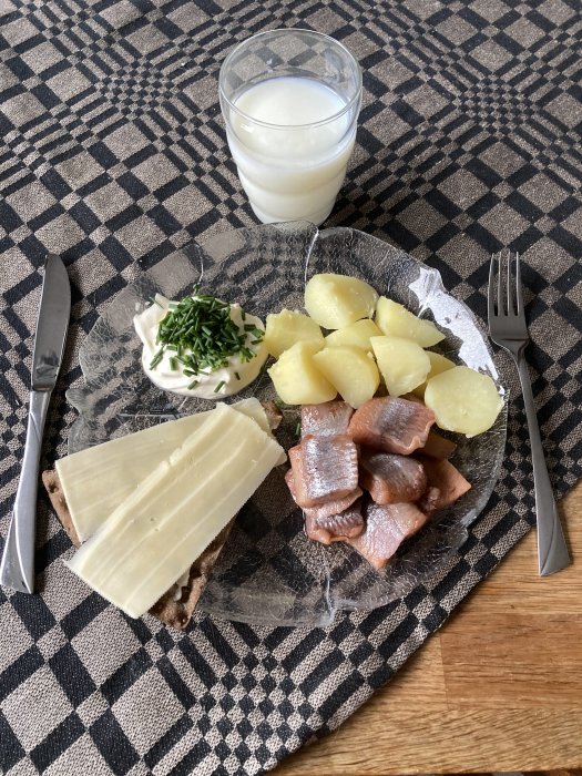 Mjölk i glas, kokt potatis, sill, kavring med ost, gräddfil med gräslök, på rutig duk.