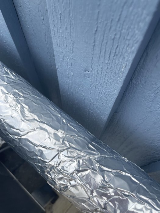 Aluminiumfolie mot blå träyta under dagsljus.