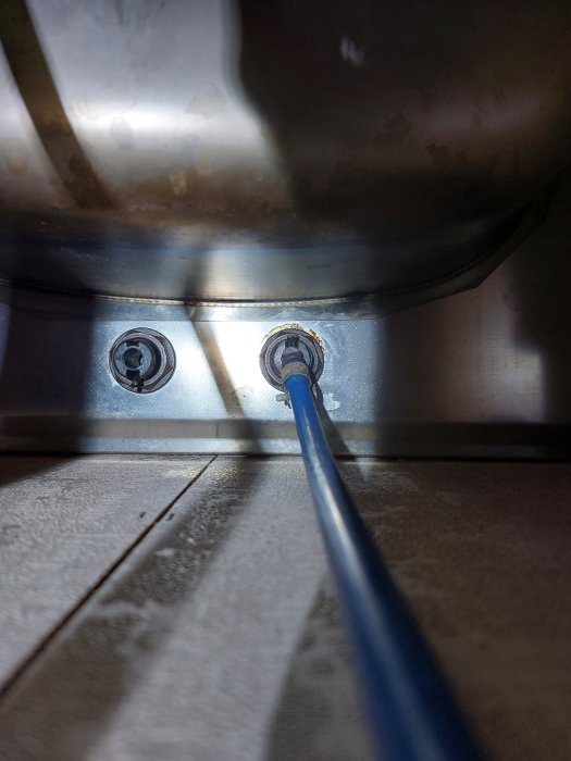 Rostfritt stål diskbänk, blå slang, vattenkran anslutning, skuggor, ljusinsläpp, närbild.
