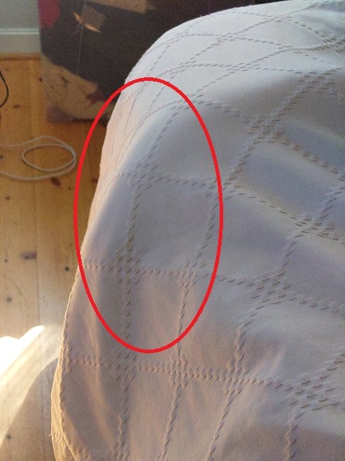 Vitt överkast med ett rött cirkelmarkerat område, trägolv, laddkabel, och en svart väska synlig.