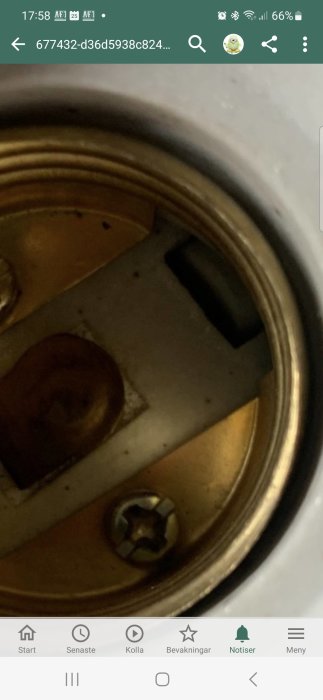 Del av en apparat, metall, möjligtvis skruv eller knapp, otydligt nedslitet, skärmbild från en smartphone.