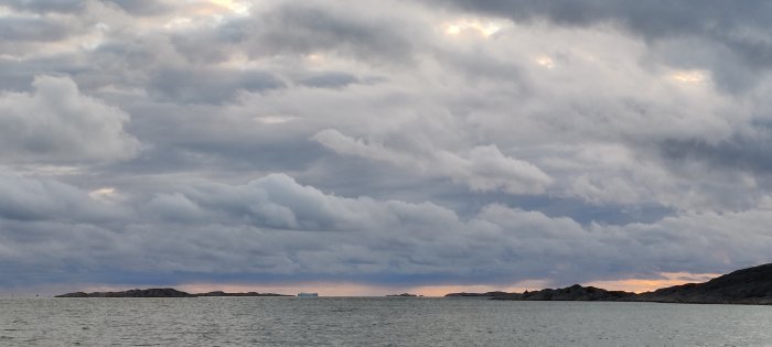 Molnig himmel över hav med öar och skimrande solnedgång i bakgrunden.