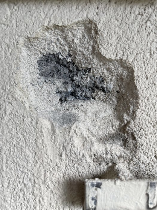 Närbild på en grov väggyta med en skada eller erosion som avslöjar mörkare material under det yttre skiktet.