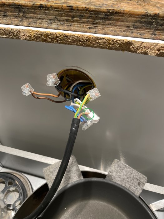 Elektriska ledningar med kopplingsklämmor i öppen väggbehållare, nära diskho och kastrull. Installationsarbete pågår.