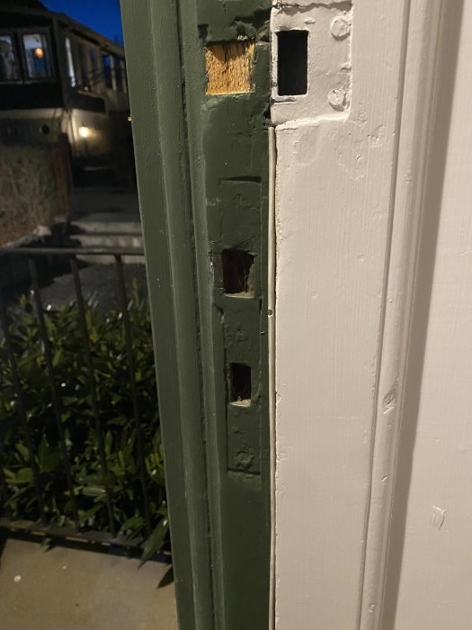 Grön och vit dörrkarm med urtag, troligen för lås, utomhus vid skymning.