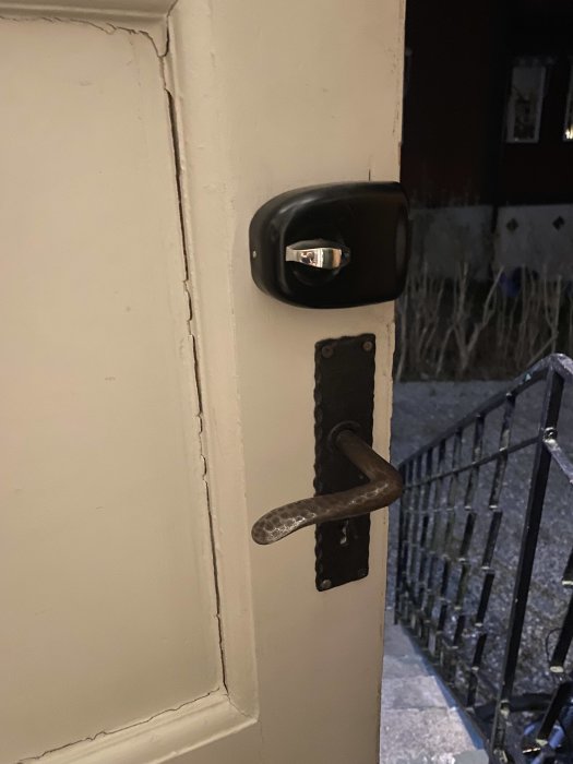 En ytterdörr med en svart digitalt kodlås ovanför en traditionell metallhandtag.