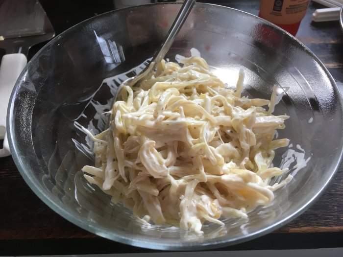 En skål med krämig coleslaw på ett mörkt bord, klastrat, transparant skål, måltidstillbehör.