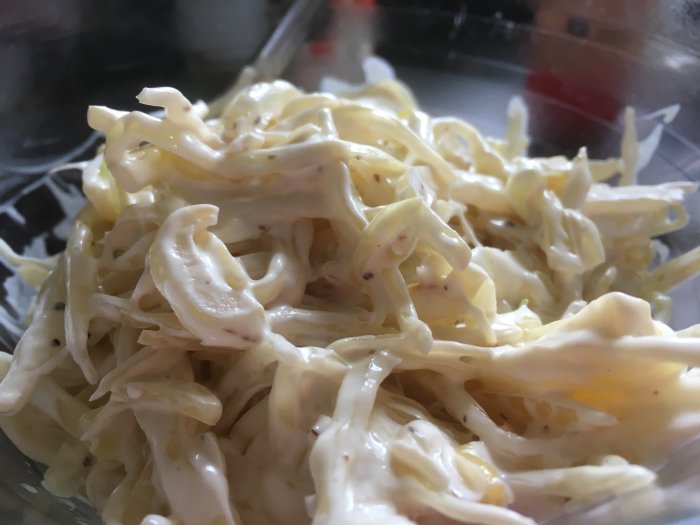 Närbild på krämig coleslaw med vitkål och majonnäs i genomskinlig behållare.