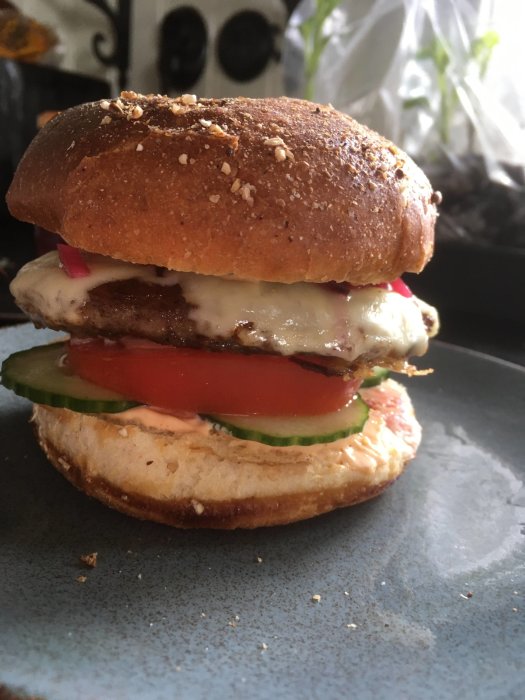 En hemlagad hamburgare med sallad, tomat, ost och dressing på ett sesambröd på en blå tallrik.