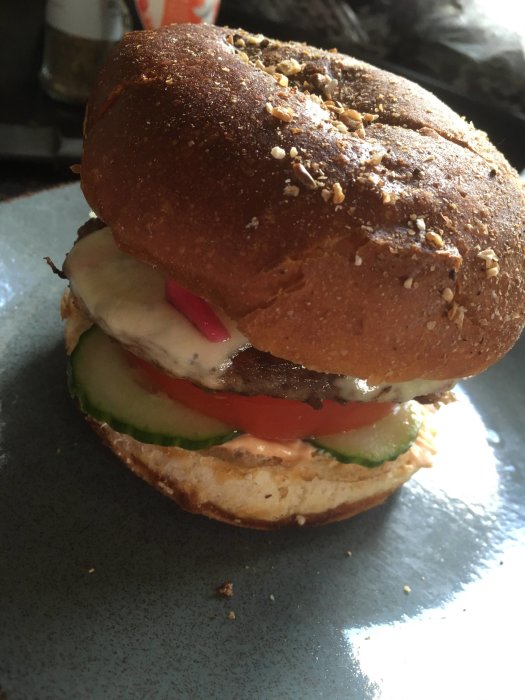 Hamburgare med sesambröd, sallad, tomat, gurka, köttpuck och dressing på en tallrik.