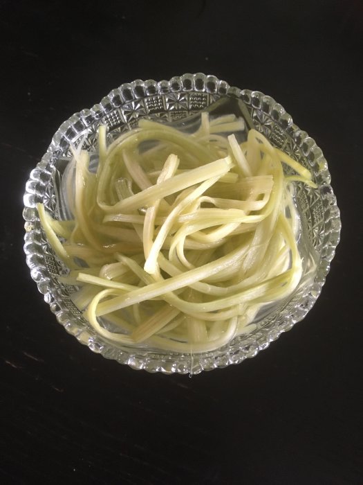 Glas-skål med tunna skivade, gröna grönsaker på mörk bakgrund. Transparent, mönstrad skålkant. Lätt och fräsch mat.