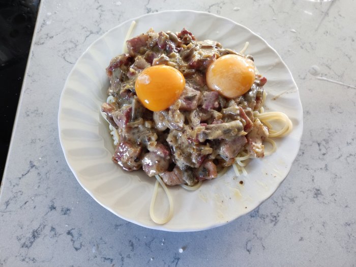 Pasta med gräddsås, bitar av kött och två råa äggulor på en tallrik.