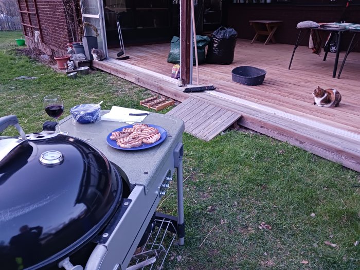 Grillfest i trädgården med vin och katter på trädäck.