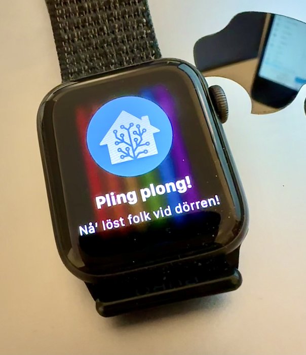 Smartklocka visar notifikation: "Pling plong! Nå't löst folk vid dörren!" med hus-ikon.