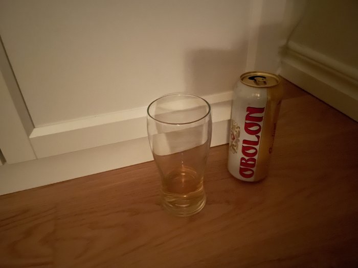 Ett glas med lite vätska, en liggande ölburk vid en dörrkarm, inomhus, nattetid.