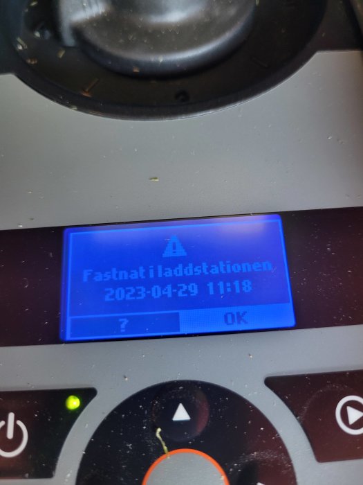 Digital display med texten "Fastnat i laddstationen, 2023-04-29 11:18", omgivet av reglage och knappar.