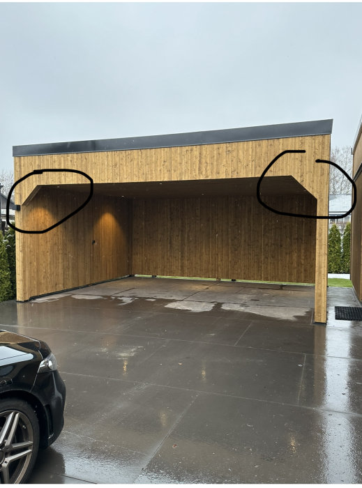 Moderna carport i trä, del av bil, våt asfalt, ringar markerade, molnig himmel.