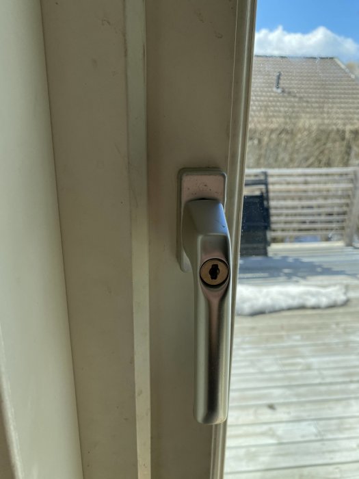 Fönsterhandtag i förgrunden, snö utomhus, del av terrass och hustak.