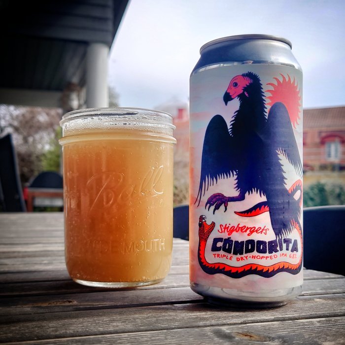 Ölburk med fantasifågel, fyllt glas på träbord utomhus, molnig himmel i bakgrunden.